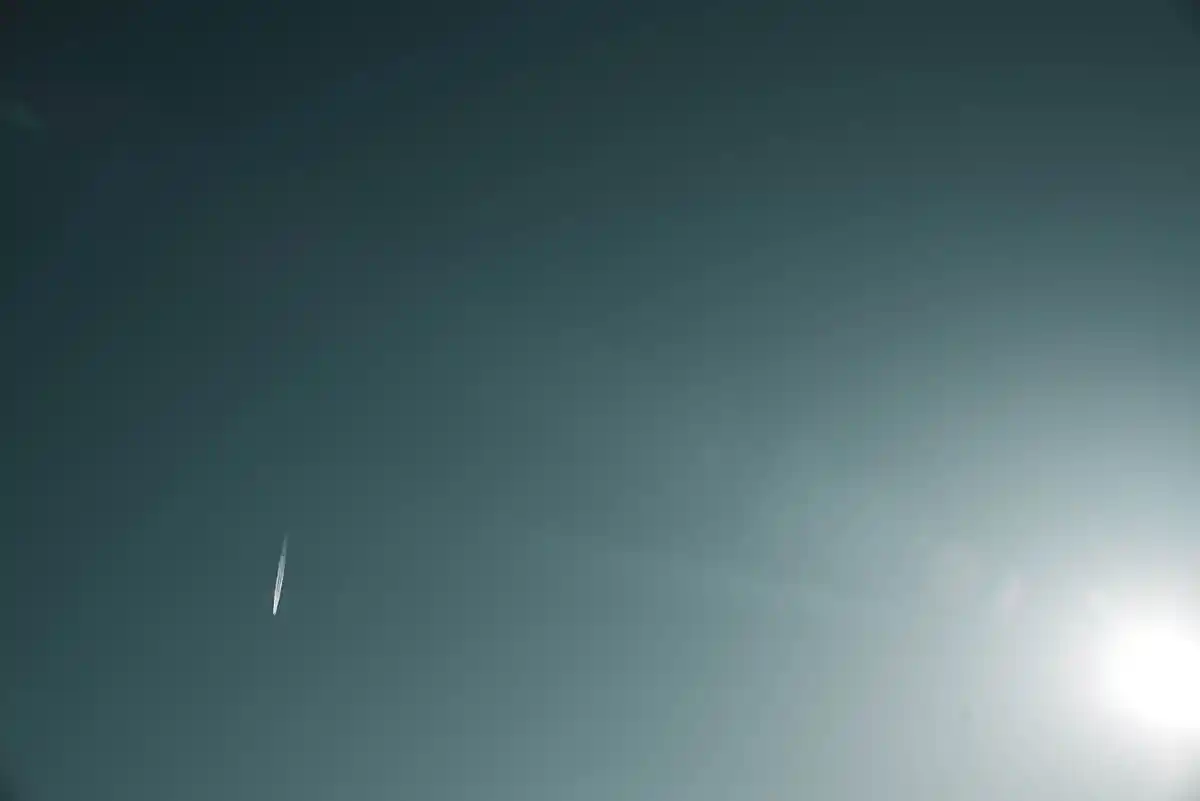 Teal sky with a bright sun flare at the right edge and a short white streak near the centre