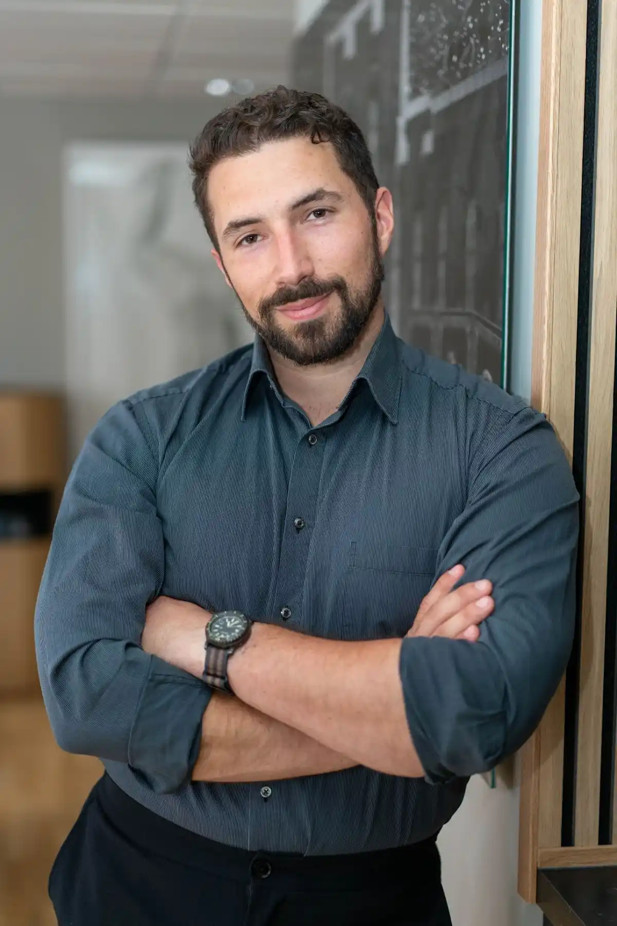 Bearded man in a blue shirt standing in a doorway with his arms folded