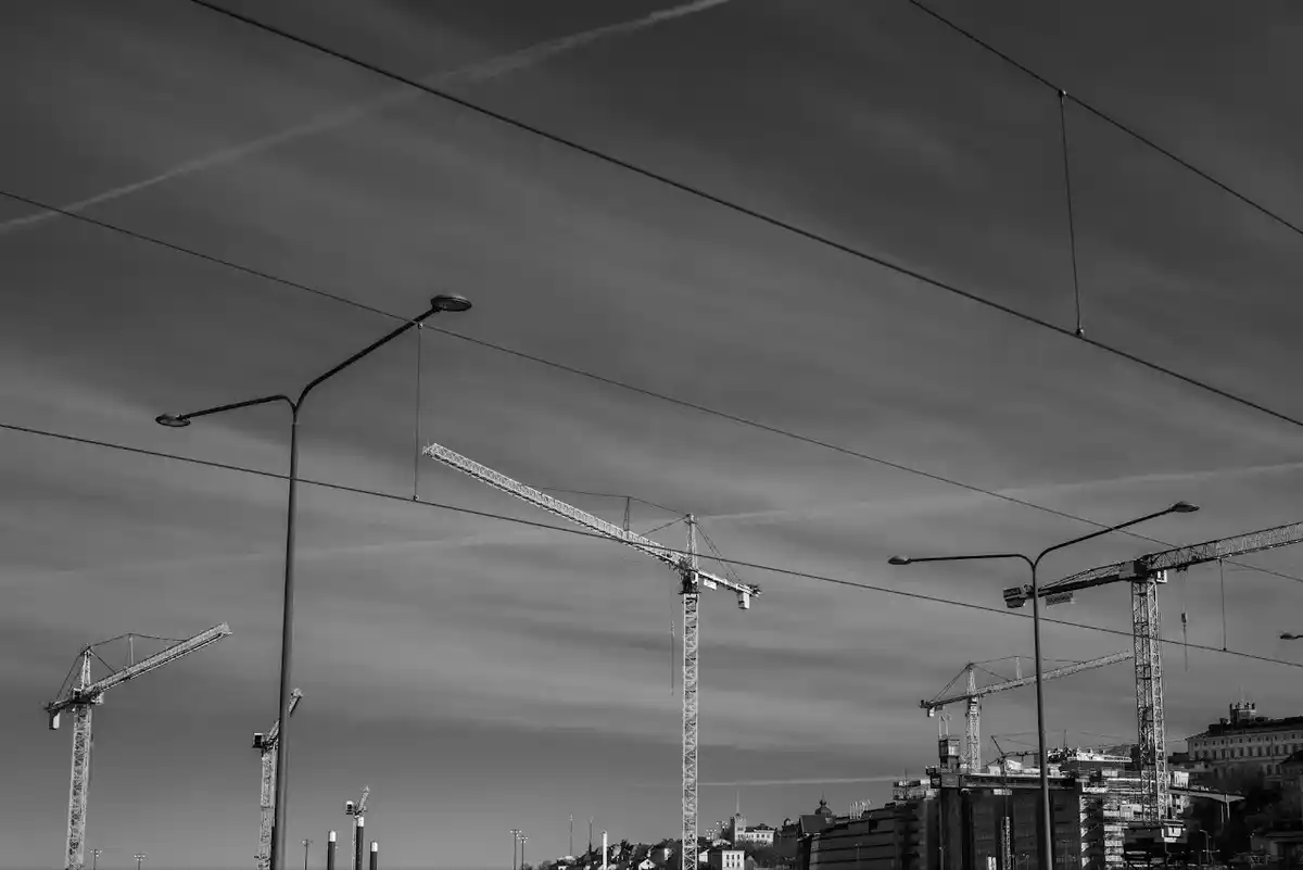 Black-and-white row of construction cranes at Slussen beneath long streaked evening clouds