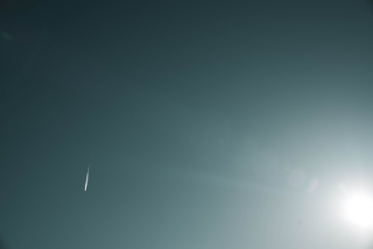 Teal sky with bright sun flare and a small white streak