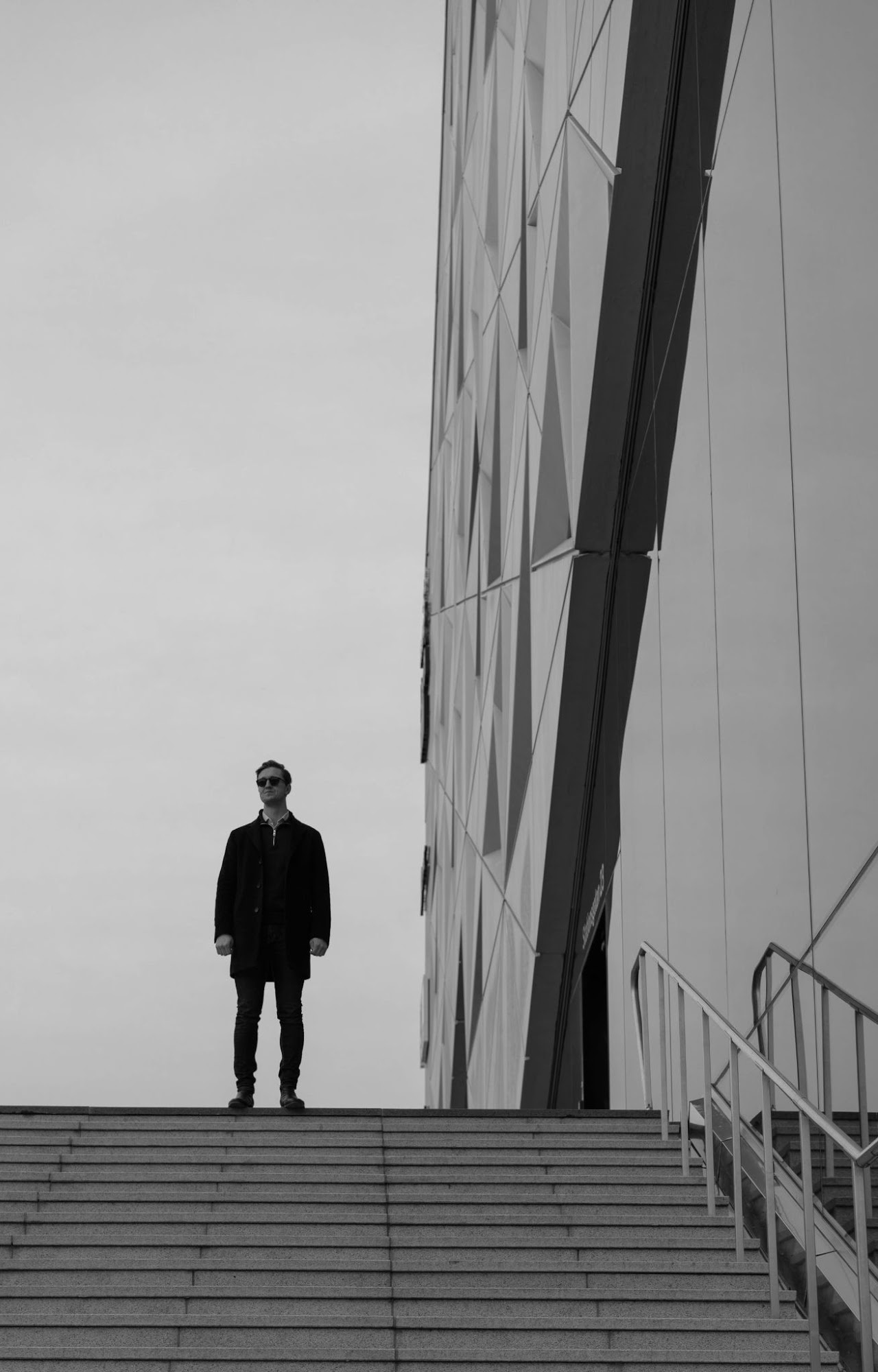 Solitary figure on steps beside a tall modern wall