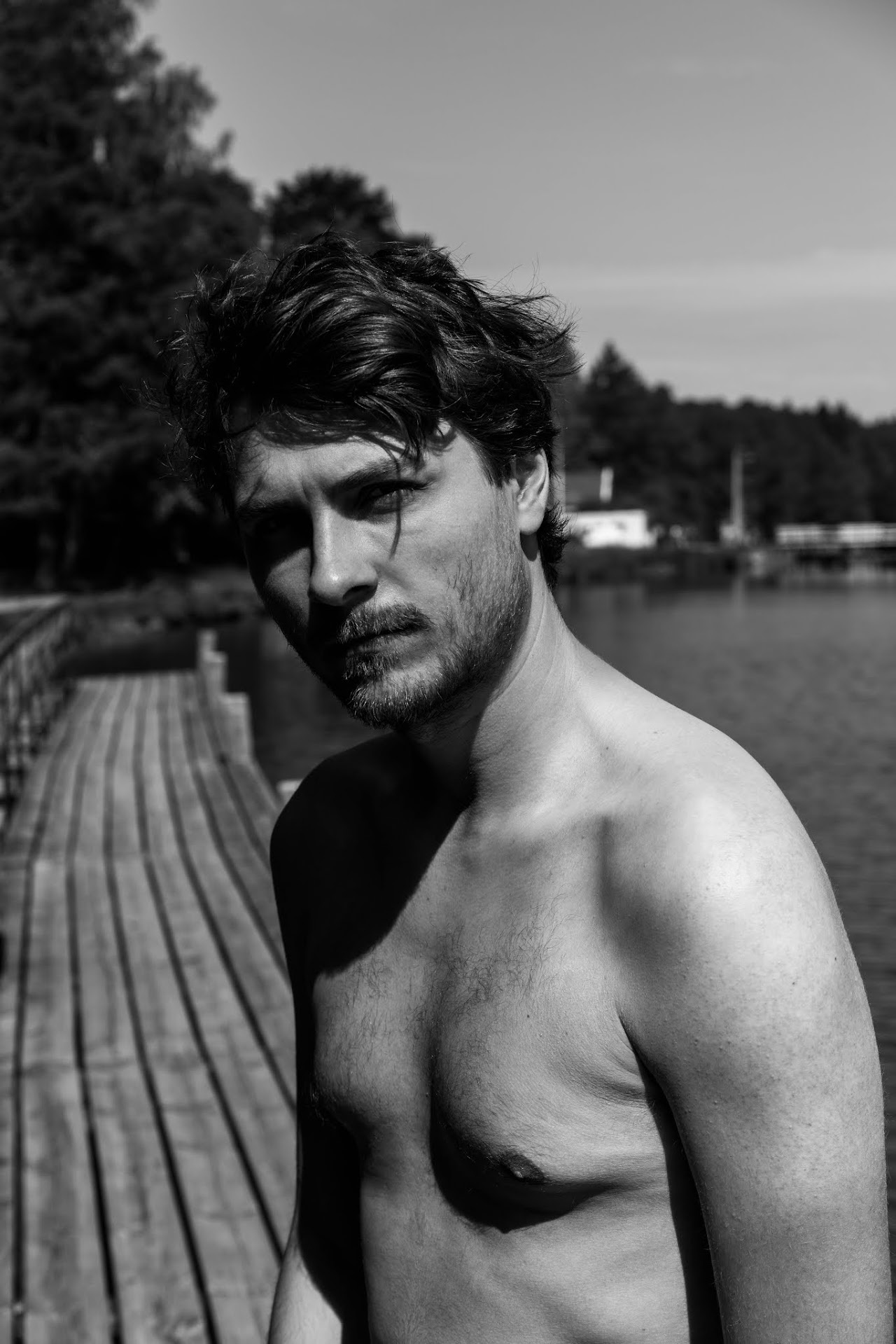 Shirtless man by a waterfront railing in black and white