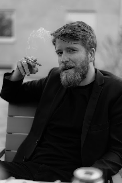 Monochrome seated bearded man holding a cigar outdoors