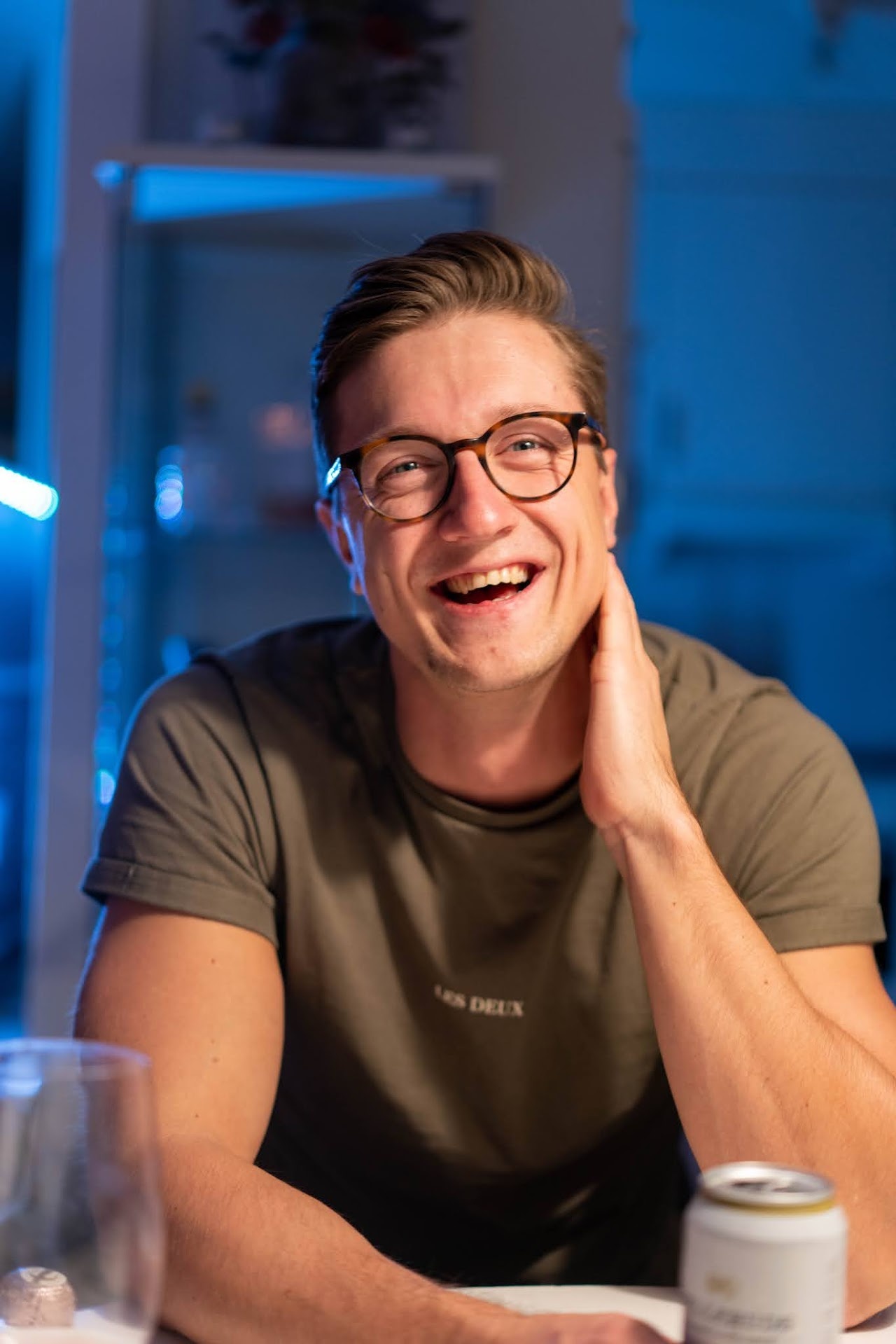 Man with glasses laughing at a table in blue evening light