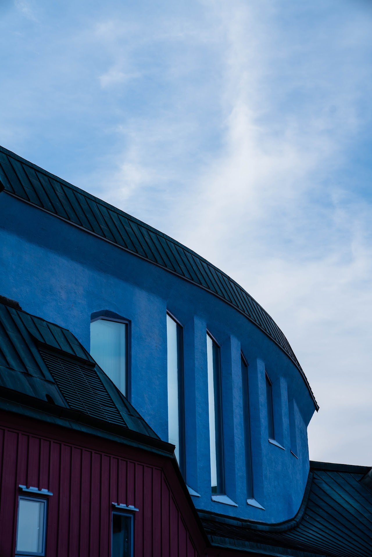 Blue rounded building facade with red lower wall and pale sky