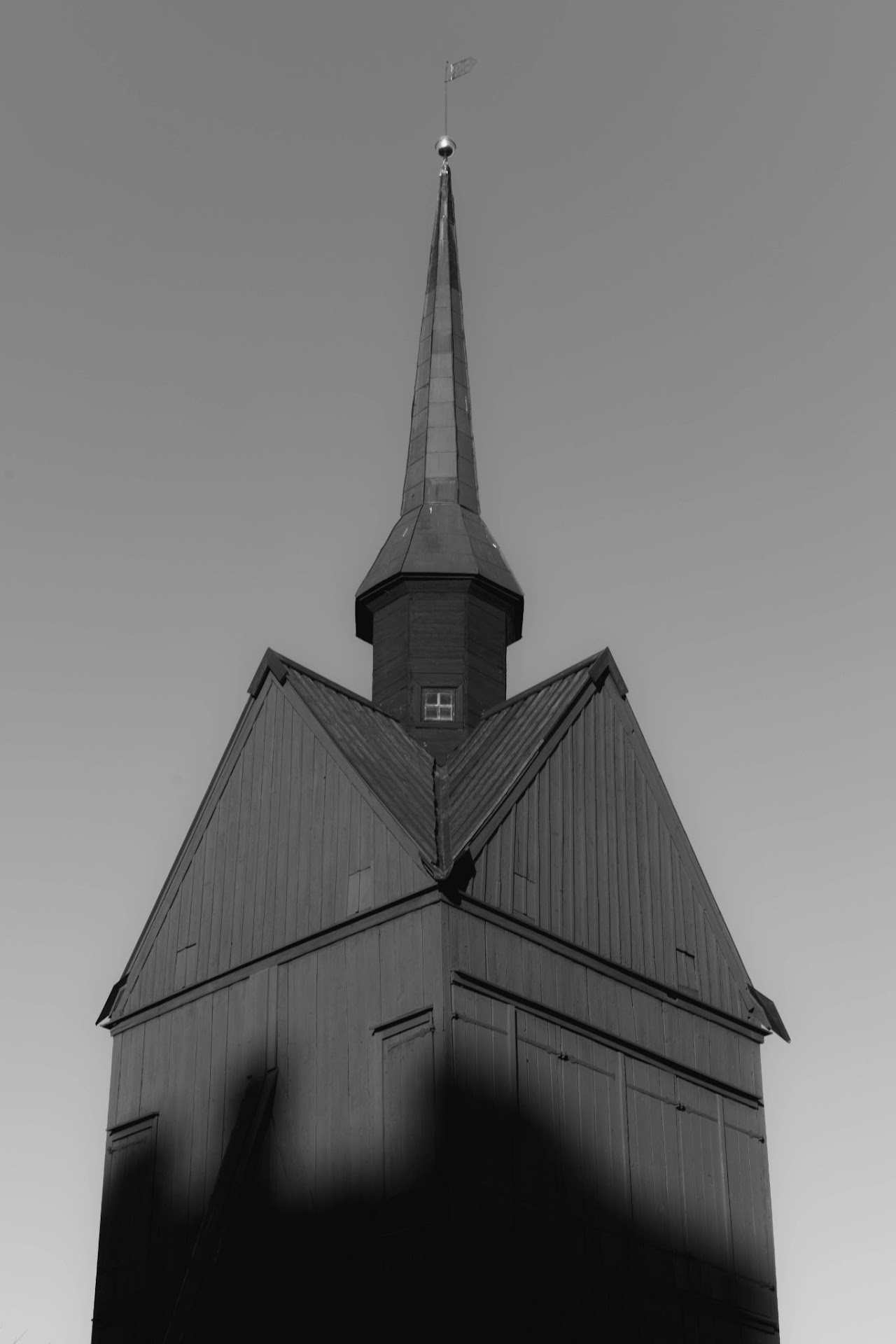 Monochrome church roof and spire rising from dark shadow